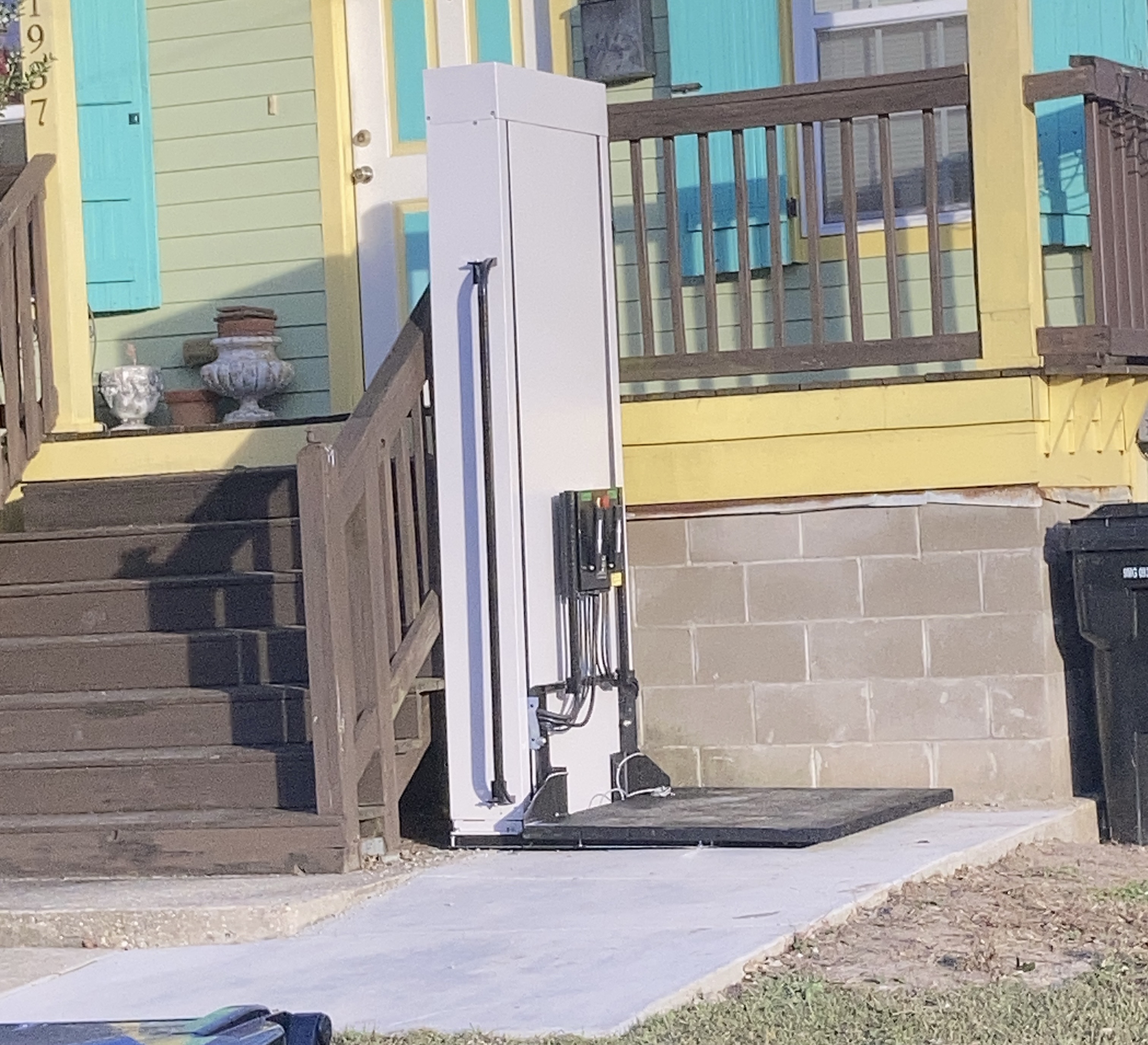 Outdoor vertical platform lift installed beside porch stairs.