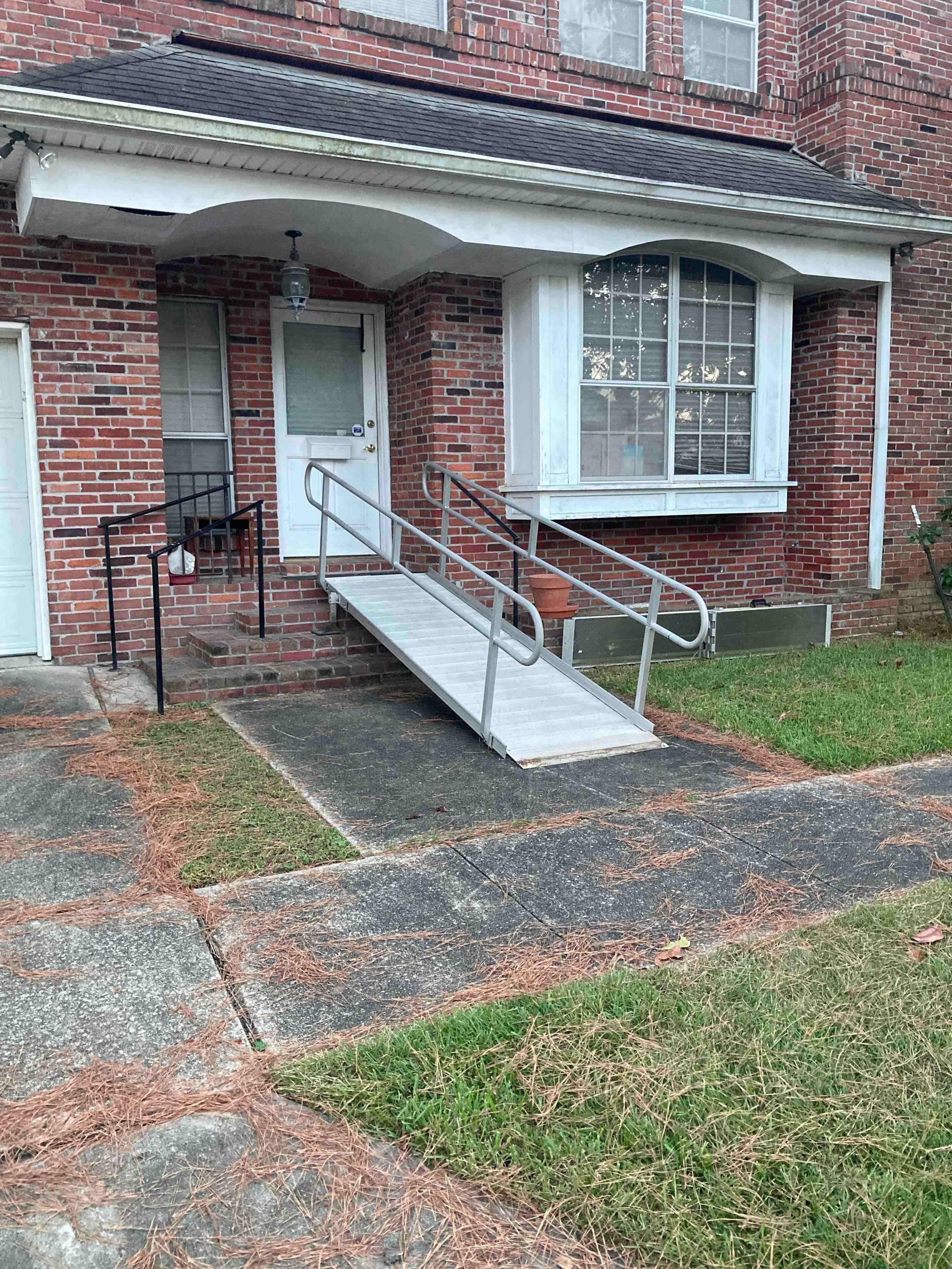 Wheelchair ramp with handrails leading to the front door of a brick home.