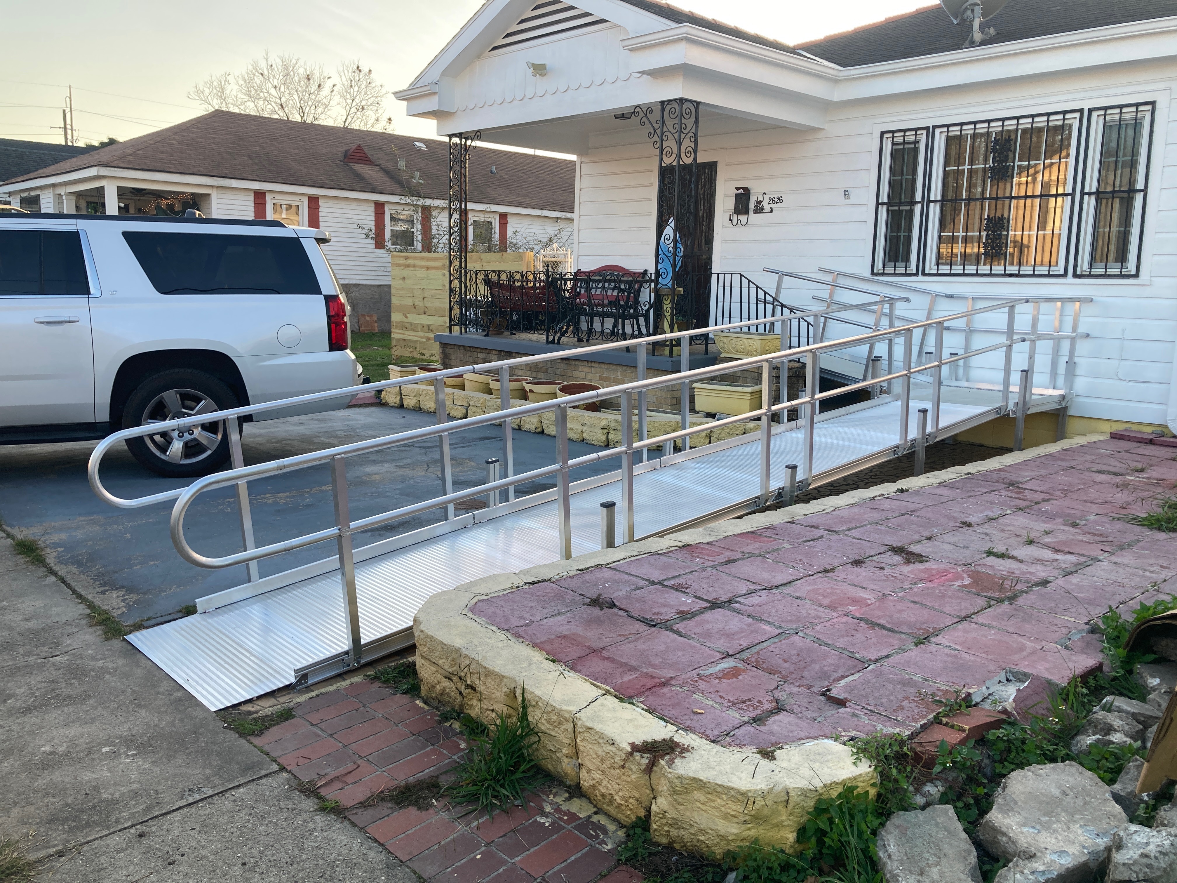 Residential aluminum wheelchair ramp with handrails leading to a porch.